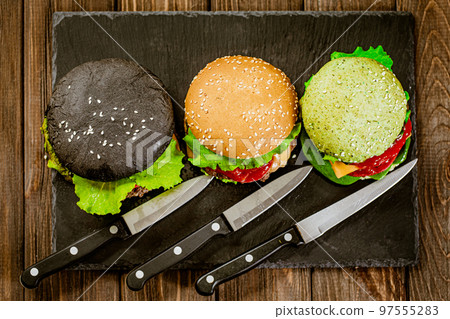 Top view of set of three color homemade burgers with marble beef with knifes on stone board. 97555283