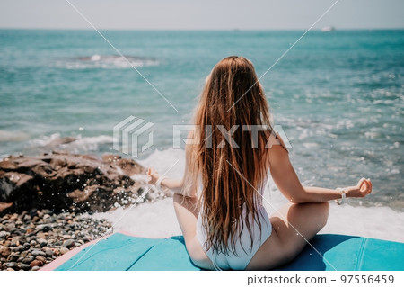 Woman yoga sea. Young woman with long hair in white swimsuit and boho style braclets practicing outdoors on yoga mat by the ocean on sunny day. Women's yoga fitness routine. Healthy lifestyle, harmony 97556459