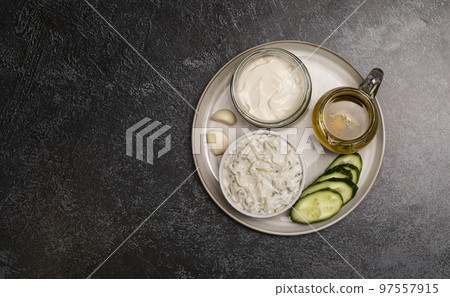 Traditional greek yogurt sauce Tzatziki,dressing in white bowl, made of grated cucumbers, sour cream yogurt,olive oil,garlic,herbs with ingredients on dark gray concrete table. Flatly, horizontal Traditional greek yogurt sauce Tzatziki,dressing in white bowl, made of grated cucumbers, sour cream yogurt,olive oil,garlic,herbs with ingredients on dark gray concrete table. Flatly, horizontal 97557915
