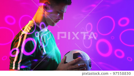 Composite of young caucasian player holding soccer ball with neon pattern in background, copy space 97558830