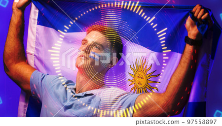 Caucasian soccer player with argentina flag paints on face waving flag over illuminated circles Caucasian soccer player with argentina flag paints on face waving flag over illuminated circles 97558897