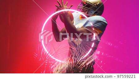 American football player catching ball while standing by illuminated circle and plants, copy space 97559221