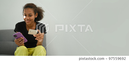 Smiling woman checking bank account on mobile phone while holding credit card in hand. Panoramic image with empty copy space 97559692