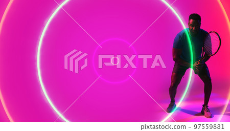African american male player holding racket and standing over illuminated circles on pink background African american male player holding racket and standing over illuminated circles on pink background 97559881