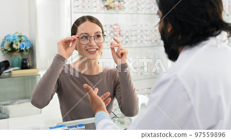 Smiling caucasian woman choosing spectacles glasses with professional optician. Eye health check and ophthalmology concept Smiling caucasian woman choosing spectacles glasses with professional optician. Eye health check and ophthalmology concept 97559896