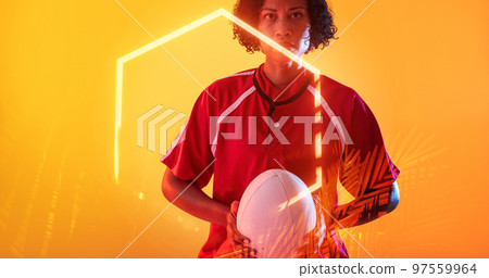 Confident biracial female player with ball and illuminated hexagon and plants on yellow background Confident biracial female player with ball and illuminated hexagon and plants on yellow background 97559964