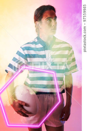 Caucasian female rugby player holding ball and standing amidst smoke over illuminated hexagon Caucasian female rugby player holding ball and standing amidst smoke over illuminated hexagon 97559985