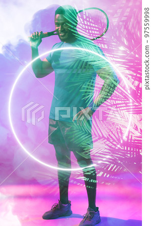 Smiling african american male tennis player holding racket over illuminated circle and plants Smiling african american male tennis player holding racket over illuminated circle and plants 97559998