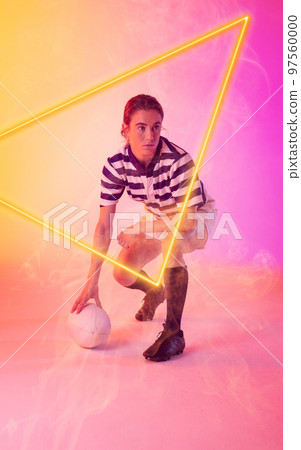 Caucasian female rugby player with ball crouching by illuminated triangle on gradient background Caucasian female rugby player with ball crouching by illuminated triangle on gradient background 97560000