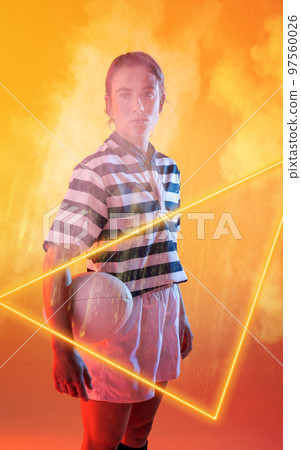 Confident female caucasian player holding ball and standing by illuminated triangle amidst smoke 97560026