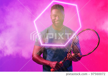 African american smiling male tennis player with racket amidst smoke by illuminated hexagon 97560072