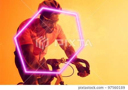 African american male cyclist wearing helmet and glasses riding bike by illuminated hexagon 97560189