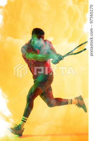 African american male tennis player hitting with racket against smoky yellow background 97560270