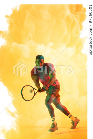 Full length of african american male player playing tennis with racket over yellow smoky background 97560301