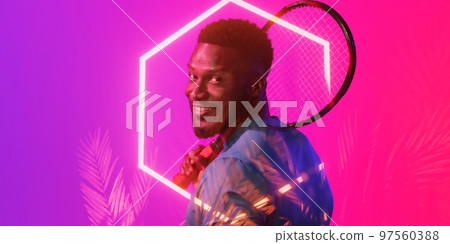 Illuminated plants and hexagon over happy african american male tennis player holding racket 97560388