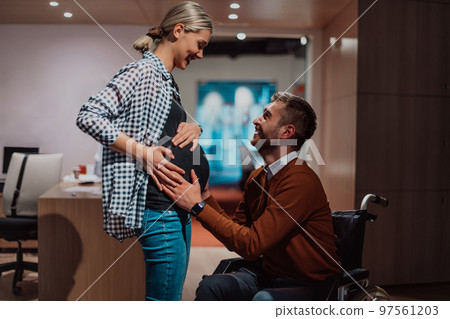 A businessman with a disability holding his pregnant wife's stomach in a modern office.  97561203