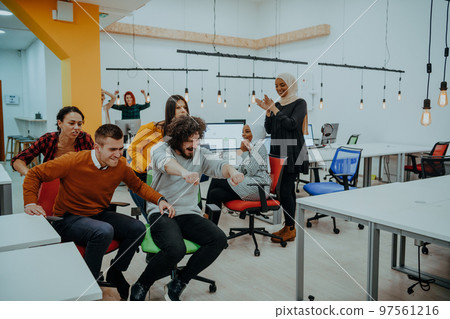 Team building and office fun. Young cheerful businesspeople in smart casual wear having fun while racing on office chairs and smiling. Team building and office fun. Young cheerful businesspeople in smart casual wear having fun while racing on office chairs and smiling. 97561216