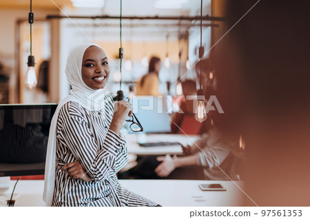 Protrait of a black ( african-american) female muslim standing in a modern business office while wearing a hijab. 97561353