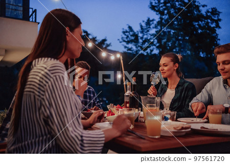 A group of young diverse people having dinner on the terrace of a modern house in the evening. Fun for friends and family. Celebration of holidays, weddings with barbecue. A group of young diverse people having dinner on the terrace of a modern house in the evening. Fun for friends and family. Celebration of holidays, weddings with barbecue. 97561720