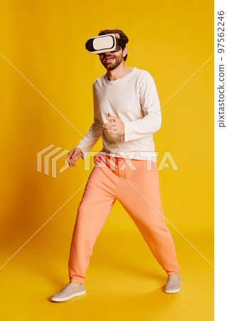 Studio footage of young Caucasian man wearing casual style clothes using VR glasses isolated over yellow background. Emotions, games, technology, ad 97562246