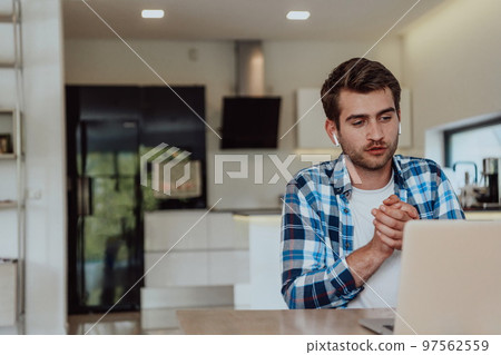 The man sitting at a table in a modern living room, with headphones using a laptop for business video chat, conversation with friends and entertainment The man sitting at a table in a modern living room, with headphones using a laptop for business video chat, conversation with friends and entertainment 97562559