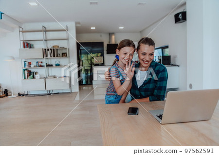 Mother with her daughter talking on laptop with family and friends while sitting in modern living room of big house Mother with her daughter talking on laptop with family and friends while sitting in modern living room of big house 97562591