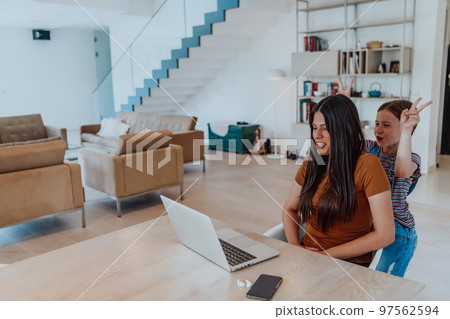 Mother with her daughter talking on laptop with family and friends while sitting in modern living room of big house Mother with her daughter talking on laptop with family and friends while sitting in modern living room of big house 97562594
