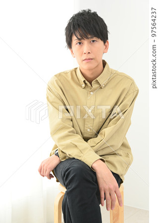 Young man portrait sitting on a chair indoors 97564237