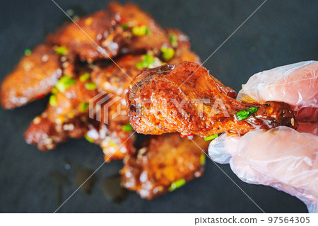 gloved hand and fried chicken with garlic and sesame in caramel on a black tray. gloved hand and fried chicken with garlic and sesame in caramel on a black tray. 97564305