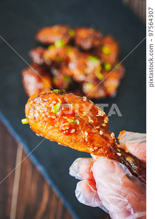 gloved hand and fried chicken with garlic and sesame in caramel on a black tray. 97564307