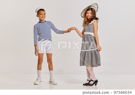 Portrait of children, boy in striped vest and teen girl in elegant dress posing over grey background. Friends Portrait of children, boy in striped vest and teen girl in elegant dress posing over grey background. Friends 97566034