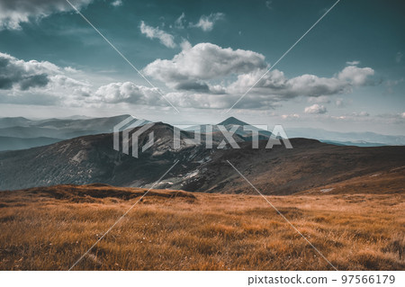 Dramatic vintage autumn mountain landscape. Incredible fall scenery. Orange grass meadow, alpine range peak, clouds in blue sky. Travel, hiking, active lifestyle. Carpathian mountains, Ukraine 97566179
