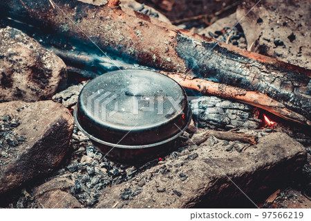 Cooking lunch or breakfast in cauldron on burning campfire in forest. Camping overnight stay stop, tourist trip in wildlife nature. Travel, trekking, hiking, tourism, lifestyle. Vintage retro toning. 97566219