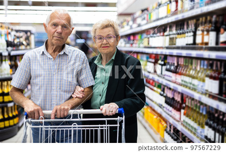 mature couple chooses bottle of wine in alcohol section of supermarket mature couple chooses bottle of wine in alcohol section of supermarket 97567229