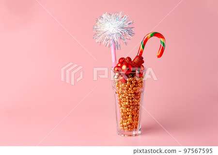 Glass with Christmas decorations on pink pastel background Glass with Christmas decorations on pink pastel background 97567595