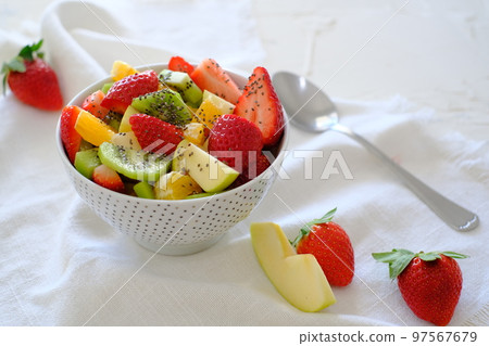Bowl of healthy fresh fruit salad on white napkin with spoon nearby Bowl of healthy fresh fruit salad on white napkin with spoon nearby 97567679