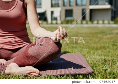 Young woman sitting in lotus position while enjoying yoga outdoors 97568047