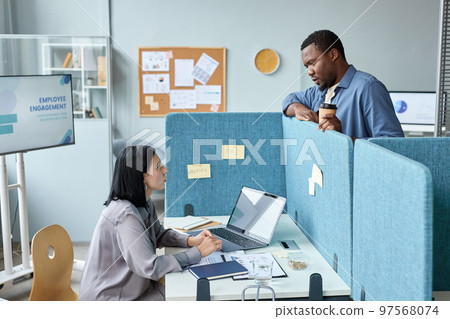 Two young colleagues talking over cubicle wall in office Two young colleagues talking over cubicle wall in office 97568074