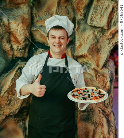 chef holds a large pizza and shows a thumb up chef holds a large pizza and shows a thumb up 97568641