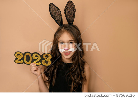 Cute beautiful long-haired girl with lacy rabbit ears holds the number 2023 of the new year Cute beautiful long-haired girl with lacy rabbit ears holds the number 2023 of the new year 97569120