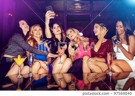 Selfie, club and women with drinks at a party for new year, birthday or festive celebration. Fun, social and friends taking picture on a phone while drinking alcohol beverage in nightclub together. Selfie, club and women with drinks at a party for new year, birthday or festive celebration. Fun, social and friends taking picture on a phone while drinking alcohol beverage in nightclub together. 97569840