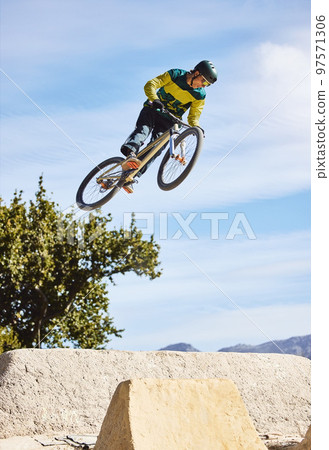Man, cyclist and mountain biking in free style, tricks or extreme hill jumping in the nature outdoors. Professional male cycling in the mountain with bicycle in the air for freedom, parkour or sports 97571306