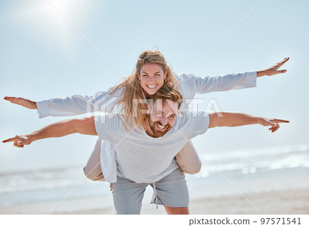 Playful, travel and couple with freedom at the beach for summer love, quality time and holiday in Costa Rica. Nature, flying piggyback and portrait of man and woman at the ocean for marriage vacation 97571541