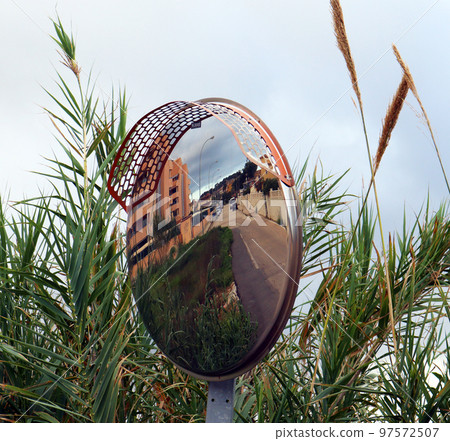 Mirror road sign among reeds, outdoor convex mirrors, traffic curved glass. Large convex mirror on the road to improve visibility. Convex mirrors for roadside safety. Mirror road sign among reeds, outdoor convex mirrors, traffic curved glass. Large convex mirror on the road to improve visibility. Convex mirrors for roadside safety. 97572507