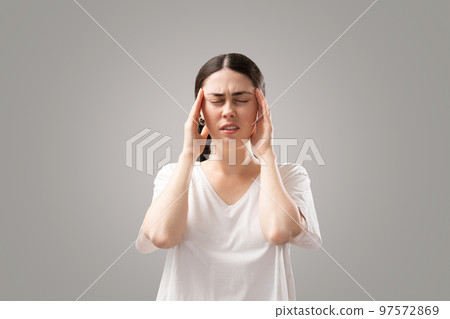 Portrait of young Caucasian woman holds her hands to her temples. Suffering from headaches and migraines. The concept of stress and psychology Portrait of young Caucasian woman holds her hands to her temples. Suffering from headaches and migraines. The concept of stress and psychology 97572869