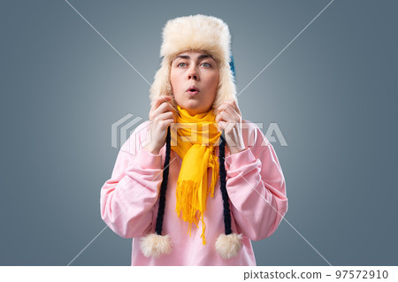 Portrait of young woman wearing knitted hat and scarf is breathing. Gray background with sofa. The concept of Illness, flu and winter season 97572910