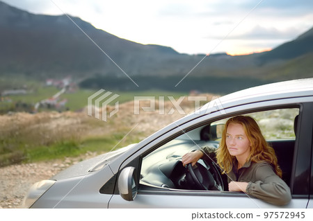 A young beautiful red-haired woman travels alone driving her car. 97572945