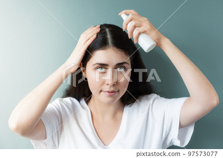 Portrait of a caucasian woman with dark hair applying spraying cosmetic product to the hair parting. Green background. The concept of hair care and dandruff problems Portrait of a caucasian woman with dark hair applying spraying cosmetic product to the hair parting. Green background. The concept of hair care and dandruff problems 97573077