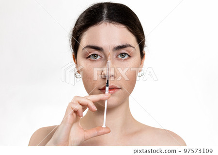 Botox and hyaluronic acid in beauty injections. Portrait of a beautiful woman holding a syringe with an injection. White background. Copy space. The concept of rejuvenation and plastic surgery Botox and hyaluronic acid in beauty injections. Portrait of a beautiful woman holding a syringe with an injection. White background. Copy space. The concept of rejuvenation and plastic surgery 97573109