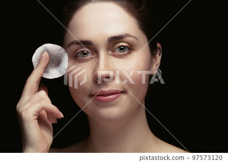 beautiful young girl holding a cotton pad around the face and a nice smile .washed off makeup.with tinted beautiful young girl holding a cotton pad around the face and a nice smile .washed off makeup.with tinted 97573120